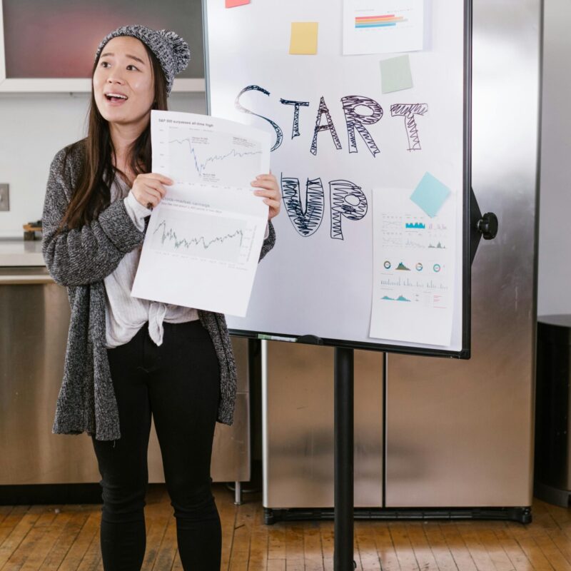 A young woman gives a startup presentation with charts and graphs on a flipchart.